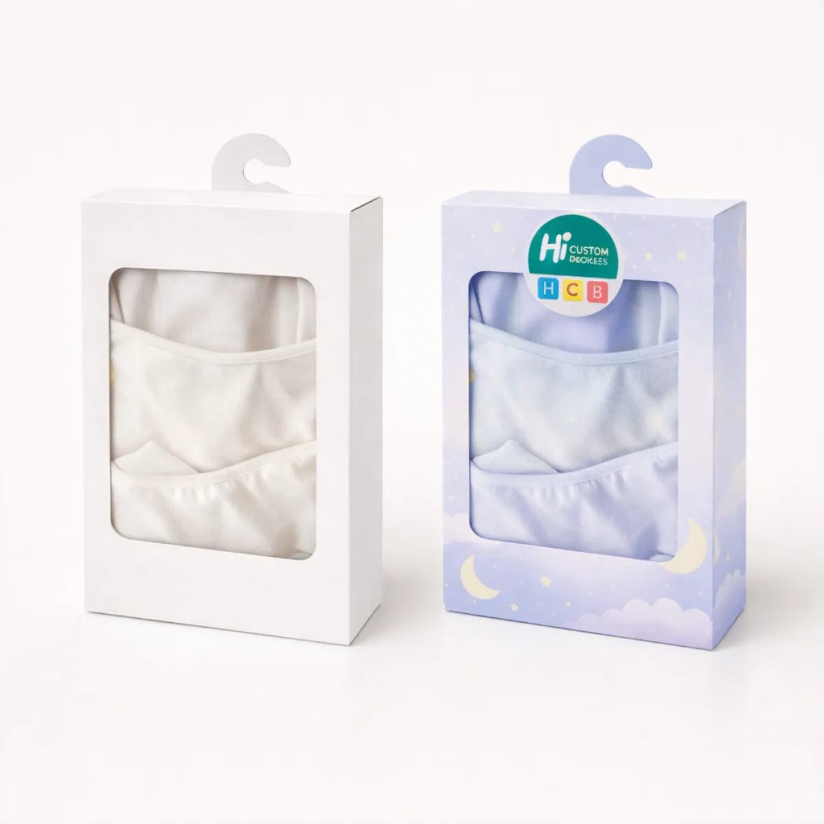 Two hanging retail boxes with windows showing folded white and light blue pyjama sets inside-